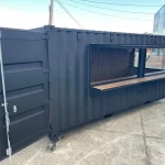 Black shipping container converted into a bar with a fold-up serving window and wood counter